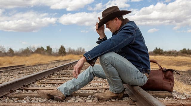 man in a cowboy hat sitting on train tracks